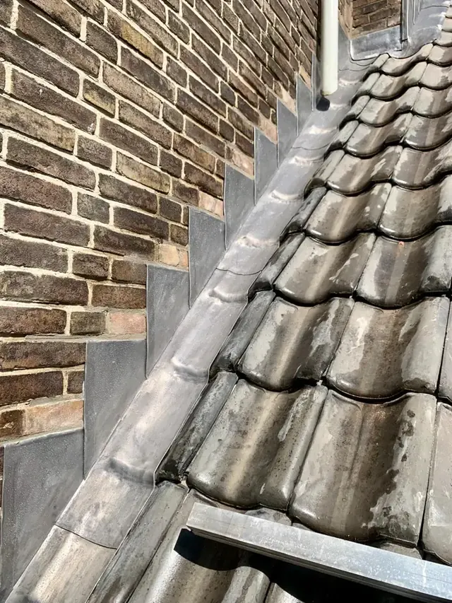 Lood langs metselwerk — De loodslabben volgen de overgang van het metselwerk naar de dakpannen.